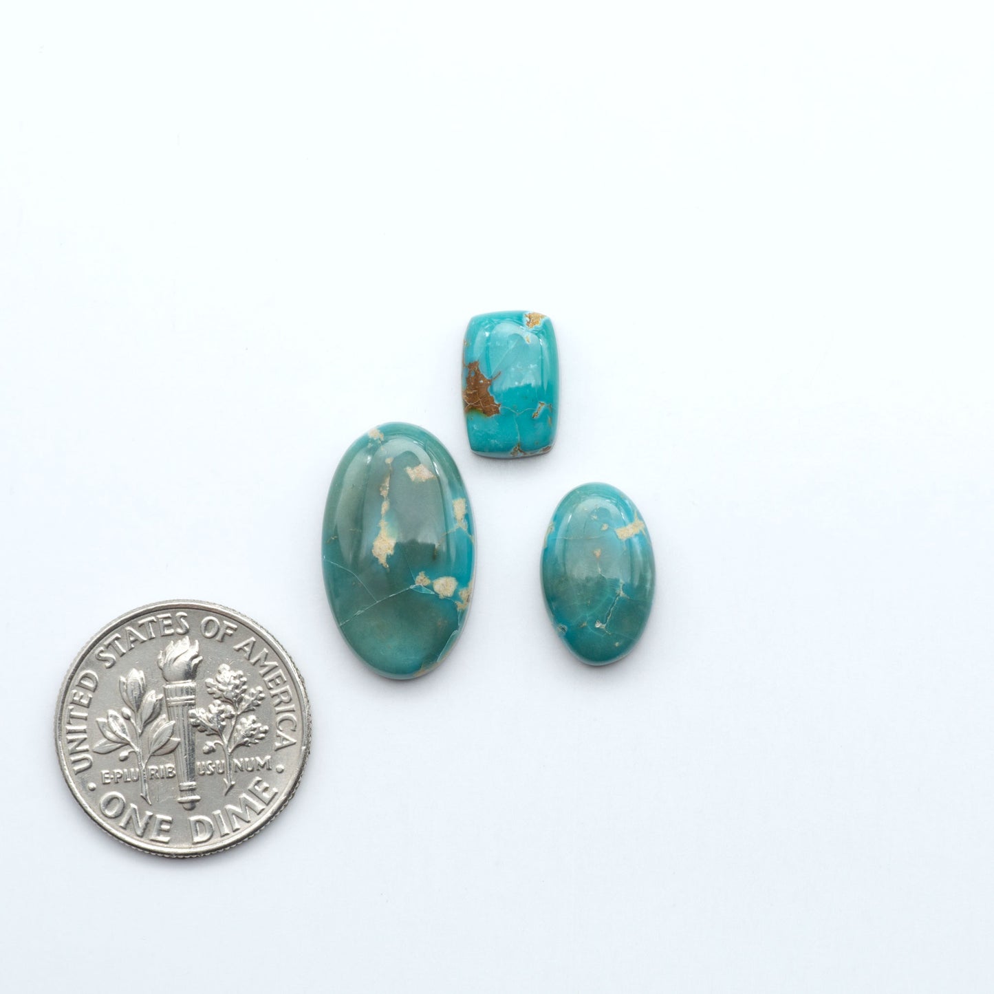 Three turquoise stones of different sizes next to a U.S. dime on a white background. Sierra Bella Turquoise cabochons feature rich blue-green color and natural matrix variation. Ideal for silversmiths, jewelers, and custom jewelry designs