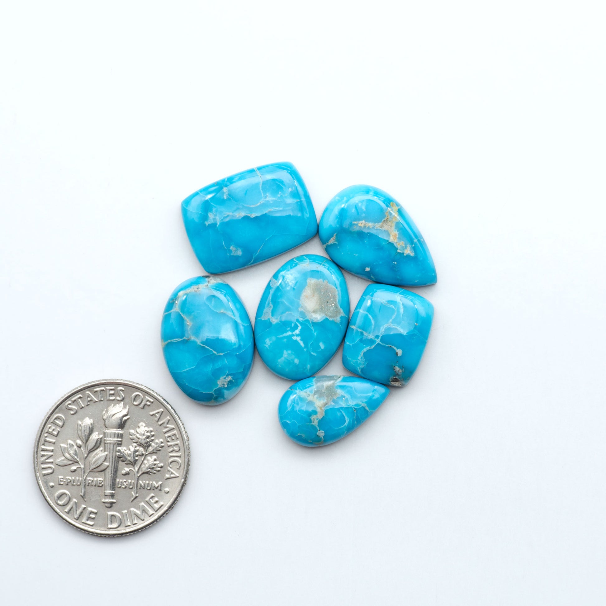 Blue turquoise stones with a U.S. dime coin for size comparison on a white background. Sierra Bella Turquoise cabochons feature rich blue-green color and natural matrix variation. Ideal for silversmiths, jewelers, and custom jewelry designs