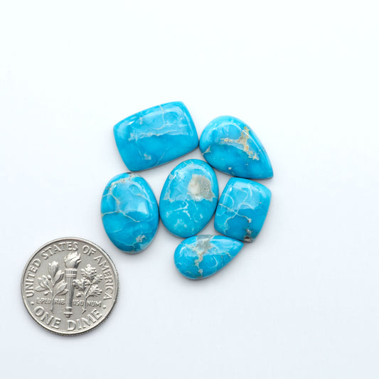 Blue turquoise stones with a U.S. dime coin for size comparison on a white background. Sierra Bella Turquoise cabochons feature rich blue-green color and natural matrix variation. Ideal for silversmiths, jewelers, and custom jewelry designs