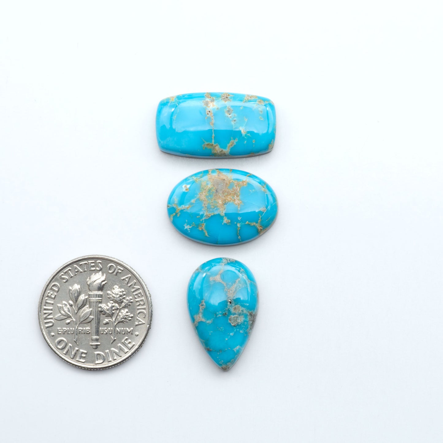 Three turquoise stones with gold veins next to a U.S. dime on a white background. Sierra Bella Turquoise cabochons feature rich blue-green color and natural matrix variation. Ideal for silversmiths, jewelers, and custom jewelry designs
