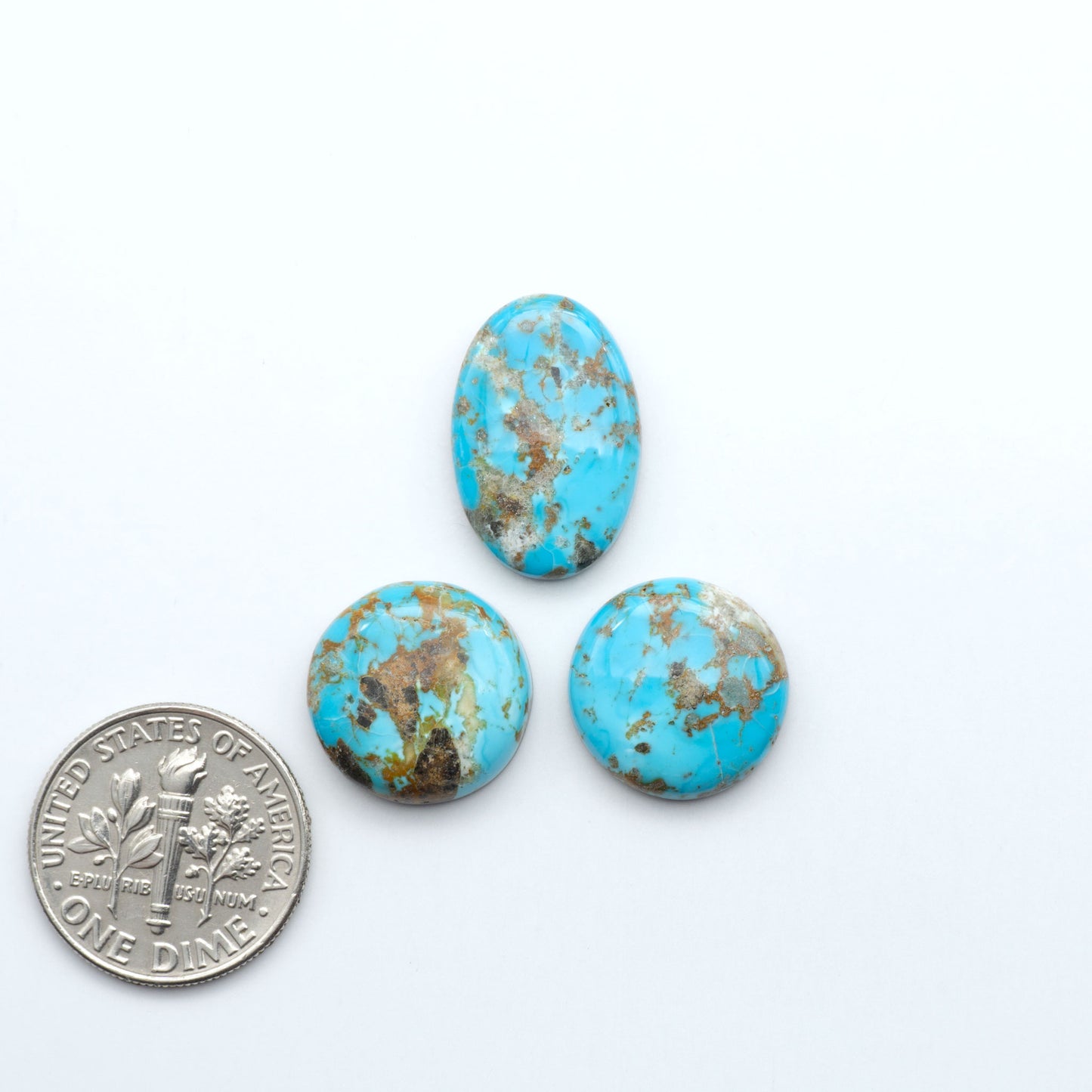 Three turquoise stones with brown matrix next to a U.S. dime on a white background. Sierra Bella Turquoise cabochons feature rich blue-green color and natural matrix variation. Ideal for silversmiths, jewelers, and custom jewelry designs