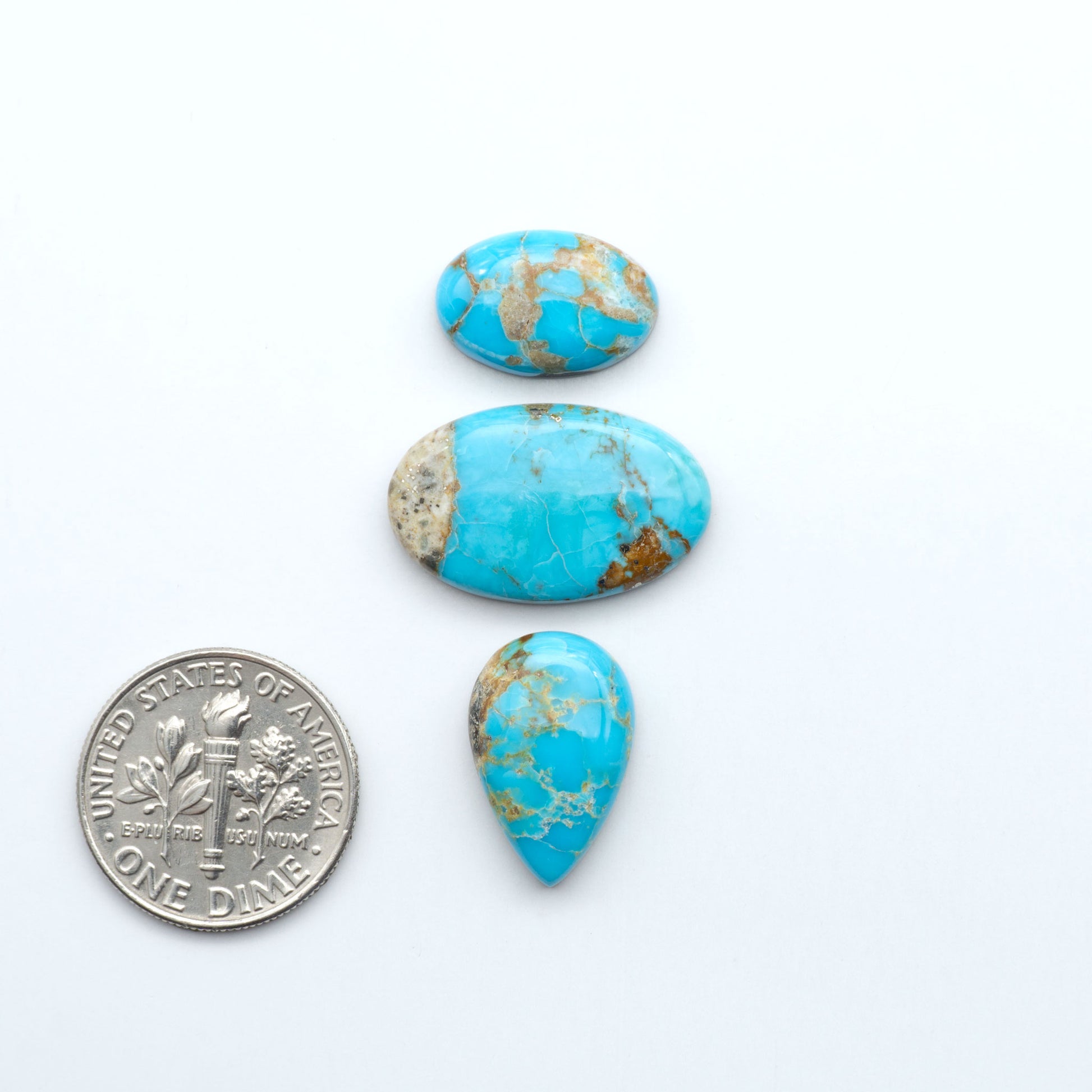 Three turquoise stones with gold veins next to a U.S. dime on a white background. Sierra Bella Turquoise cabochons feature rich blue-green color and natural matrix variation. Ideal for silversmiths, jewelers, and custom jewelry designs