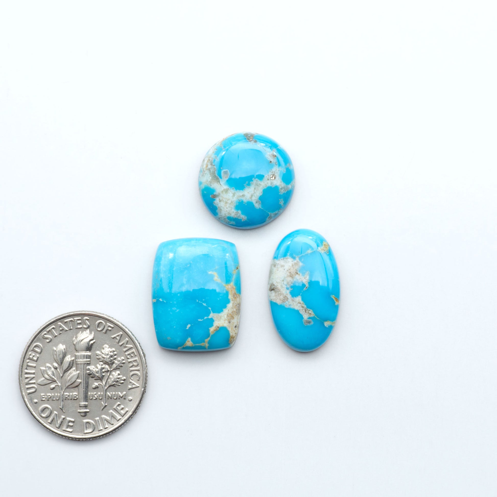 Three blue marbled stones with gold flecks next to a U.S. dime on a white background. Sierra Bella Turquoise cabochons feature rich blue-green color and natural matrix variation. Ideal for silversmiths, jewelers, and custom jewelry designs