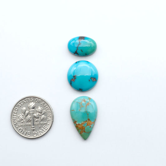 Three turquoise stones with gold veins on a white background, one next to a U.S. dime for size comparison. Sierra Bella Turquoise cabochons feature rich blue-green color and natural matrix variation. Ideal for silversmiths, jewelers, and custom jewelry designs