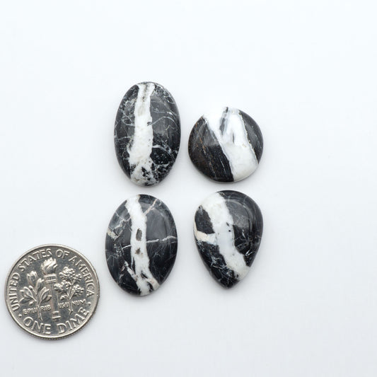 Four black and white marbled stones with a U.S. dime for scale on a white background.Natural White Buffalo Stone Cabochons are semi-precious gemstones cut into shapes ideal for jewelry-making, making them an excellent choice for artisans.