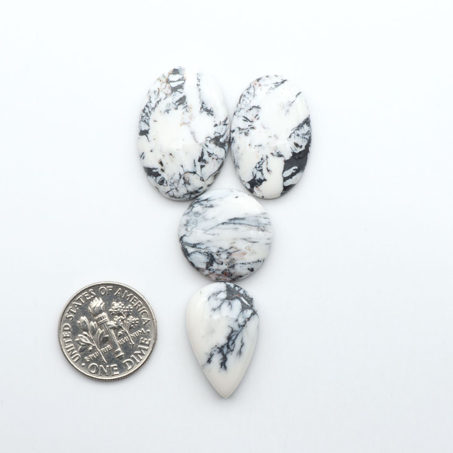Marble-patterned stones with a U.S. dime for scale on a white background Natural White Buffalo Stone Cabochons are semi-precious gemstones cut into shapes ideal for jewelry-making, making them an excellent choice for artisans.