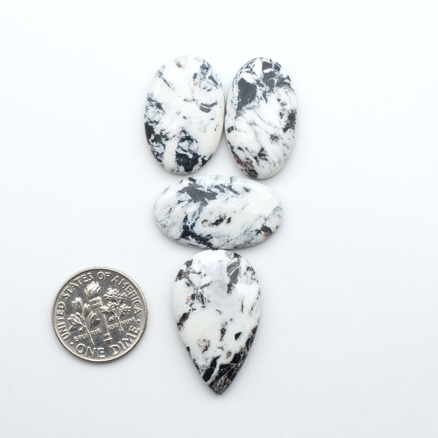Four marbled stones of different shapes on a white background with a quarter for scale. Natural White Buffalo Stone Cabochons are semi-precious gemstones cut into shapes ideal for jewelry-making, making them an excellent choice for artisans.