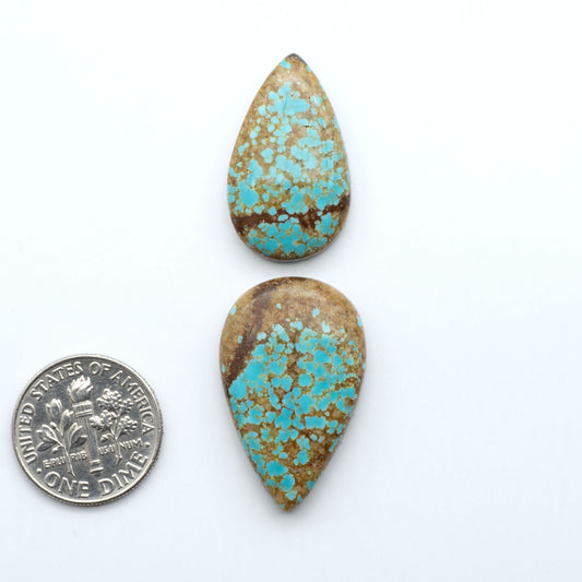 Two turquoise stones with brown speckles next to a U.S. quarter on a white background Number 8 Turquoise Cabochons have been selected for their quality and unique appearance. Don't miss the chance to add a one-of-a-kind piece to your collection.