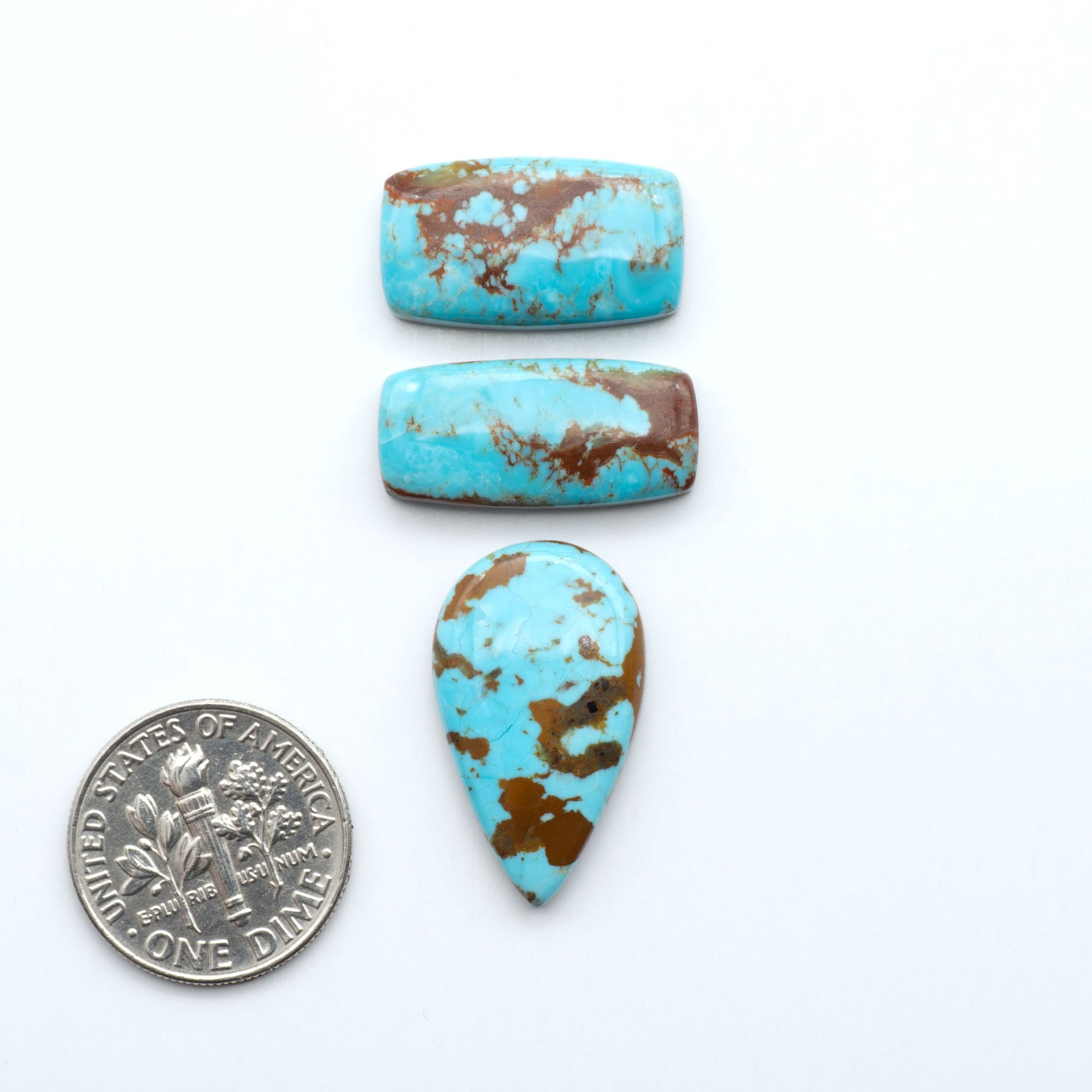Three turquoise stones with brown speckles on a white background, one next to a dime for size comparison. Number 8 Turquoise Cabochons have been selected for their quality and unique appearance. Don't miss the chance to add a one-of-a-kind piece to your collection.
