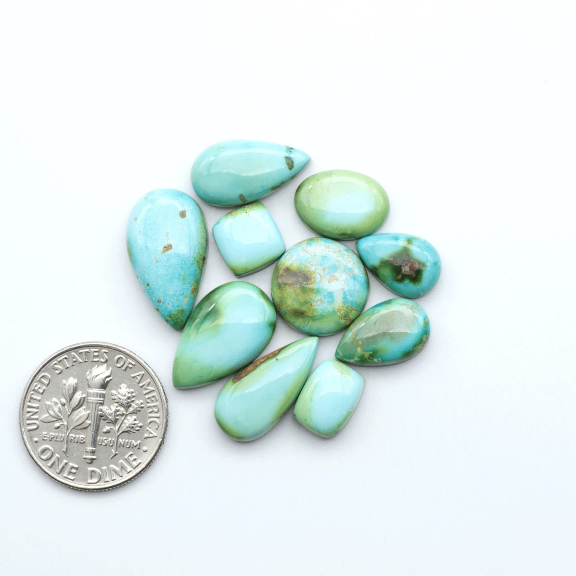 Turquoise stones with a U.S. dime for scale on a white background. Sonoran Mountain Turquoise showcases a stunning blend of blue and green hues and natural patterns that make it a must-have for any jewelry collection.