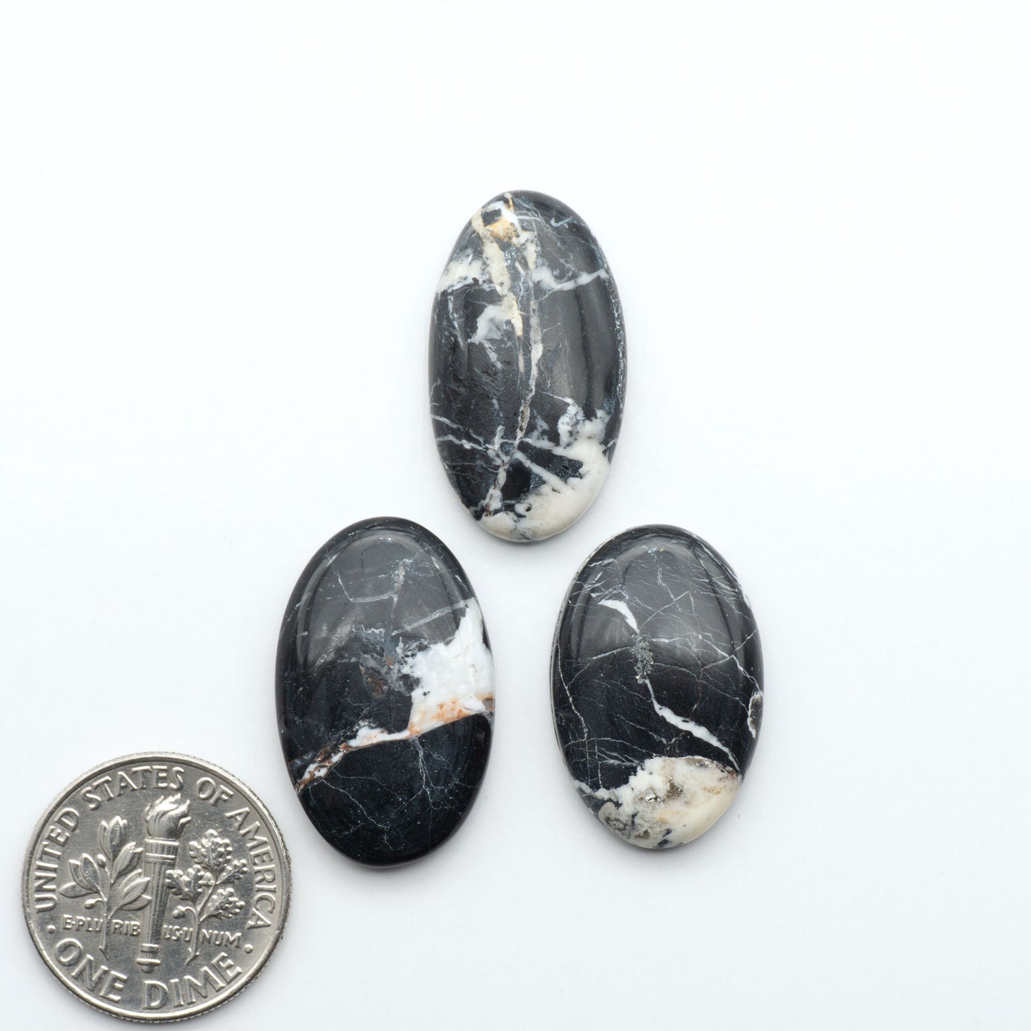 Three oval black and white marbled stones with a quarter for scale on a white background Natural White Buffalo Stone Cabochons are semi-precious gemstones cut into shapes ideal for jewelry-making, making them an excellent choice for artisans.
