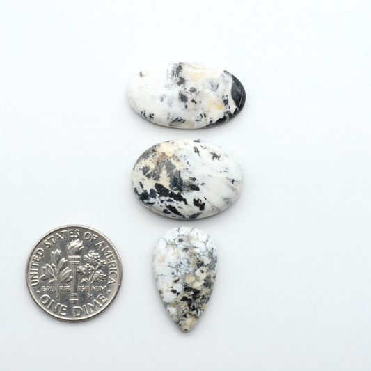Three teardrop-shaped marbled stones next to a U.S. dime on a white background Natural White Buffalo Stone Cabochons are semi-precious gemstones cut into shapes ideal for jewelry-making, making them an excellent choice for artisans.
