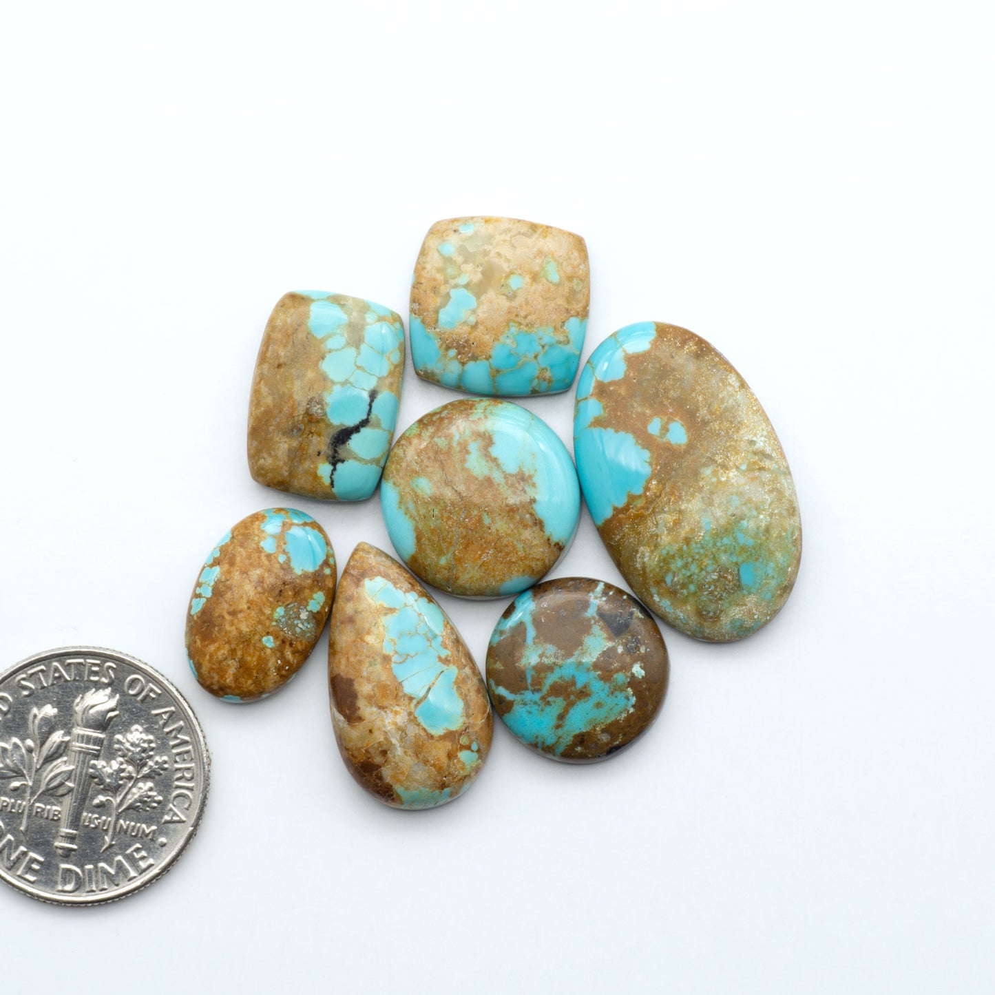 Turquoise stones with a quarter for scale on a white background. Number 8 Turquoise Cabochons have been selected for their quality and unique appearance. Don't miss the chance to add a one-of-a-kind piece to your collection.