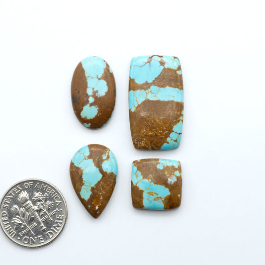 Four turquoise stone beads with brown matrix on a white background, one next to a U.S. quarter for size comparison. Number 8 Turquoise Cabochons have been selected for their quality and unique appearance. Don't miss the chance to add a one-of-a-kind piece to your collection.