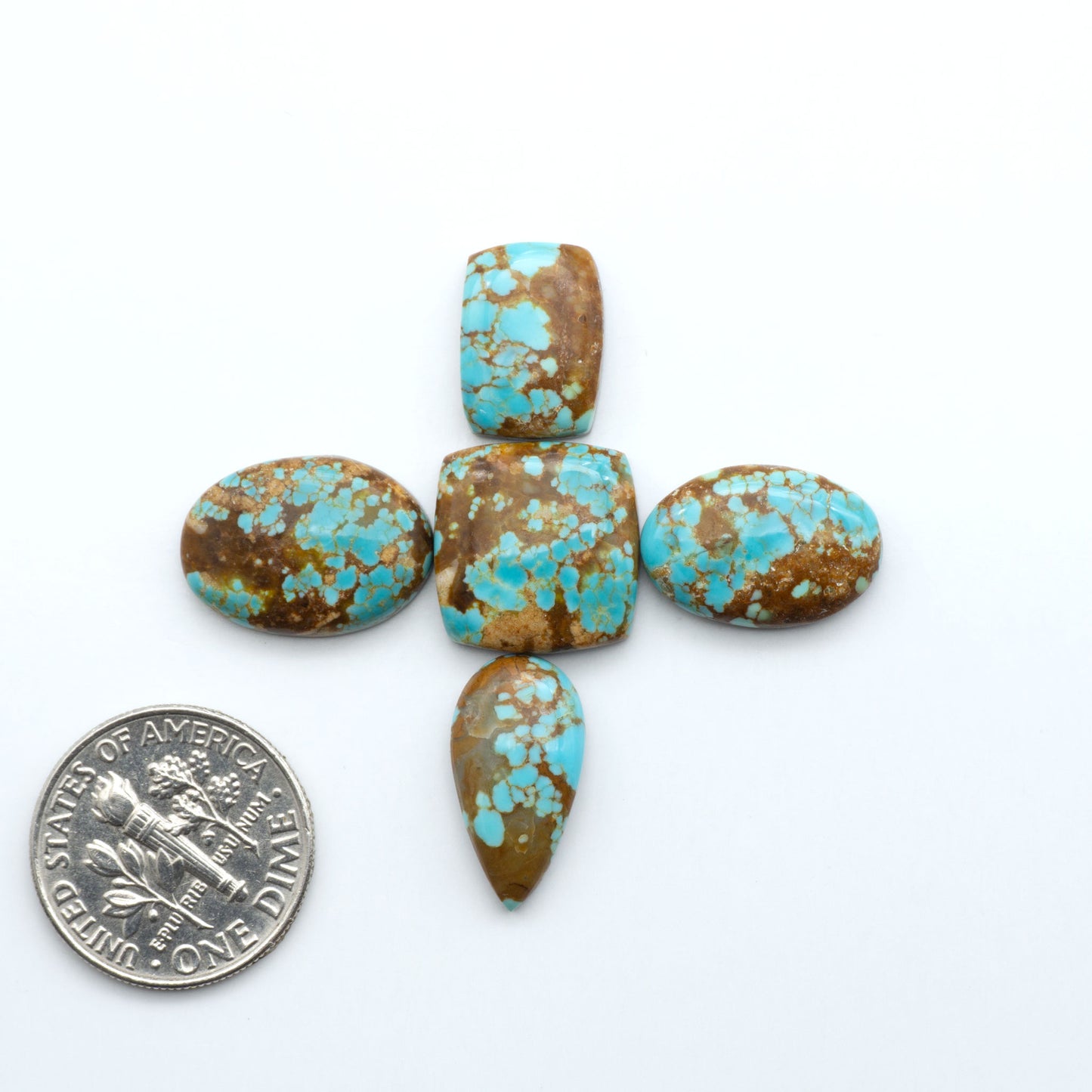 Turquoise stones on a white background with a quarter for scale. Number 8 Turquoise Cabochons have been selected for their quality and unique appearance. Don't miss the chance to add a one-of-a-kind piece to your collection.