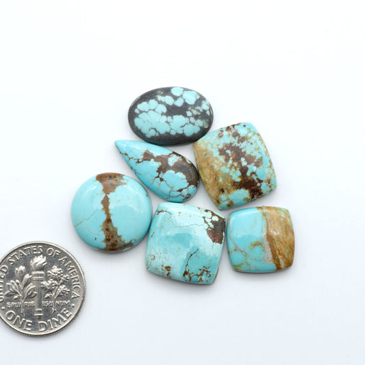 Turquoise stones with brown accents on a white background, one next to a dime for size comparison. Number 8 Turquoise Cabochons have been selected for their quality and unique appearance. Don't miss the chance to add a one-of-a-kind piece to your collection.