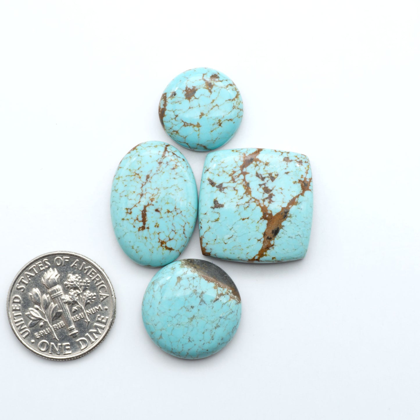 Four turquoise stones with brown speckles on a white background, one coin for scale. Number 8 Turquoise Cabochons have been selected for their quality and unique appearance. Don't miss the chance to add a one-of-a-kind piece to your collection.