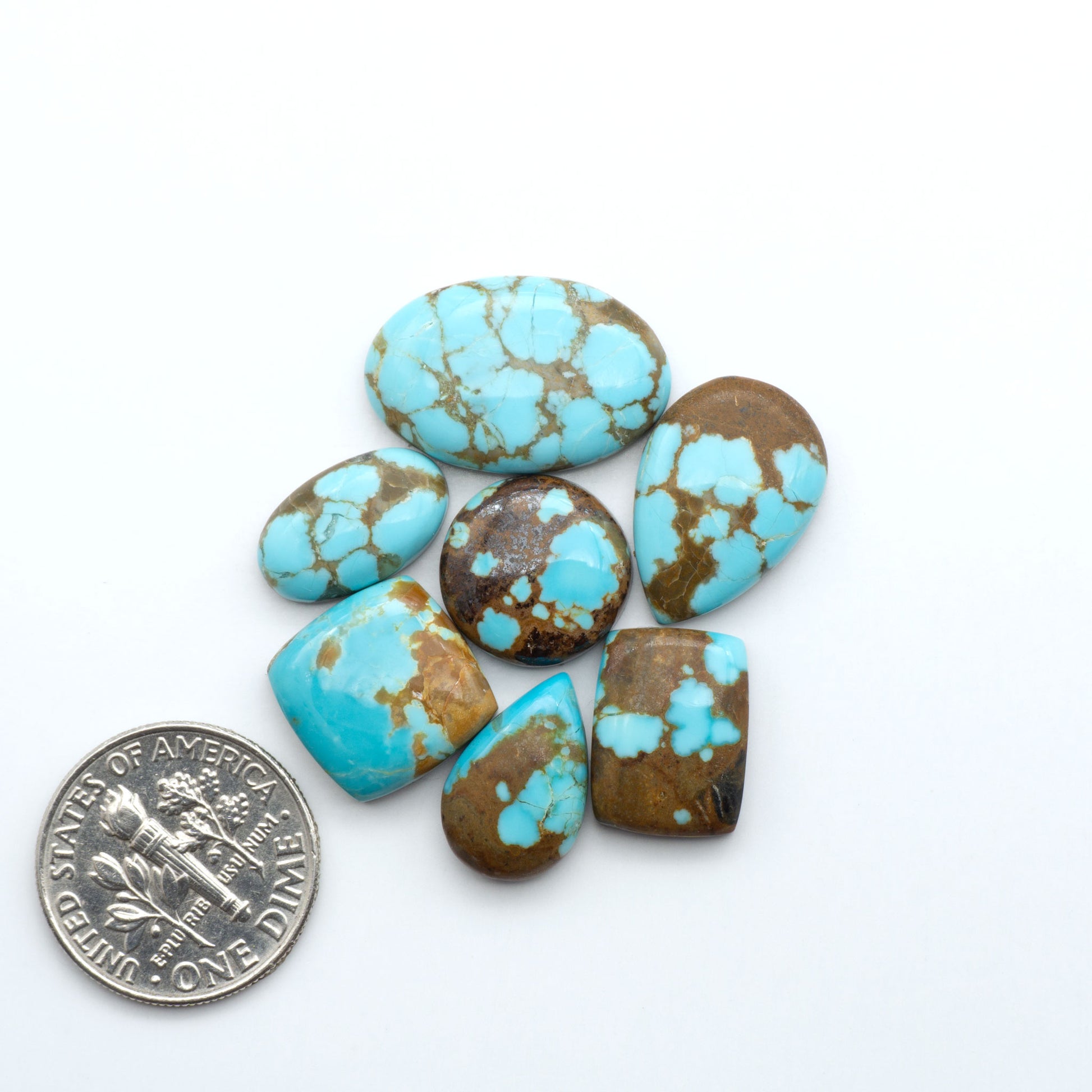 Turquoise stones with brown accents on a white background, one next to a dime for size comparison. Number 8 Turquoise Cabochons have been selected for their quality and unique appearance. Don't miss the chance to add a one-of-a-kind piece to your collection.
