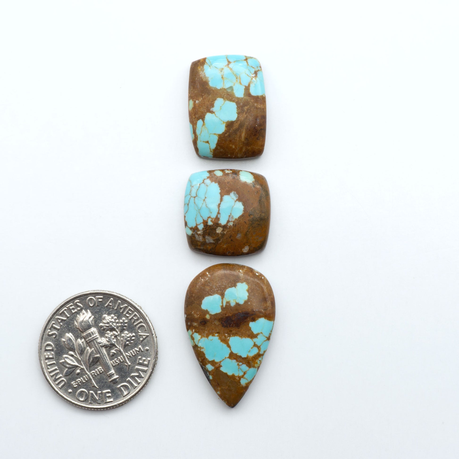 Three turquoise stones of different shapes and sizes on a white background with a dime for scale. Number 8 Turquoise Cabochons have been selected for their quality and unique appearance. Don't miss the chance to add a one-of-a-kind piece to your collection.