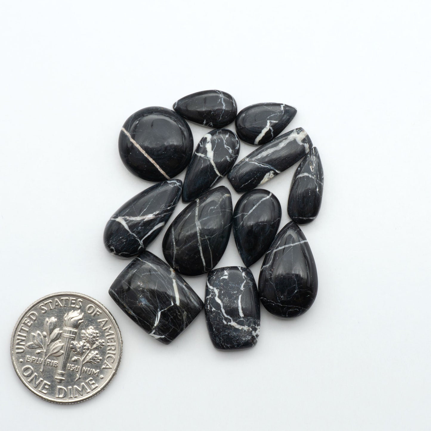 Black marbled stones with a quarter for scale on a white background. Natural White Buffalo Stone Cabochons are semi-precious gemstones cut into shapes ideal for jewelry-making, making them an excellent choice for artisans.
