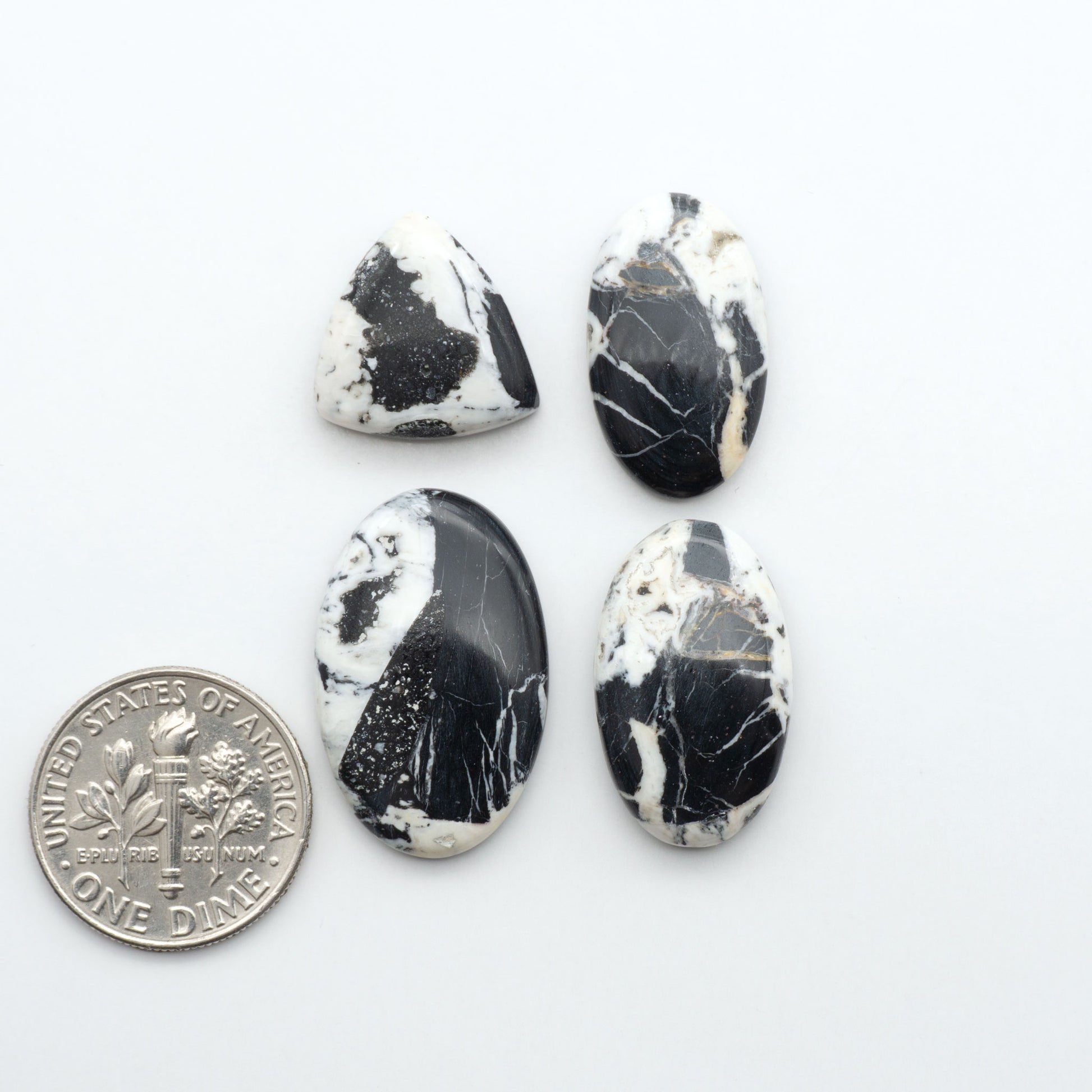Four black and white marbled stones with a quarter for scale on a white background. Natural White Buffalo Stone Cabochons are semi-precious gemstones cut into shapes ideal for jewelry-making, making them an excellent choice for artisans.
