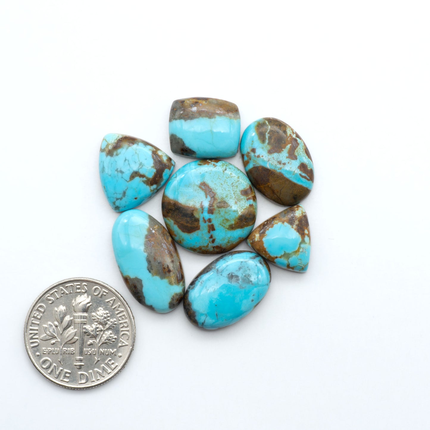 Turquoise stones with a U.S. dime for size comparison on a white background. Number 8 Turquoise Cabochons have been selected for their quality and unique appearance. Don't miss the chance to add a one-of-a-kind piece to your collection.