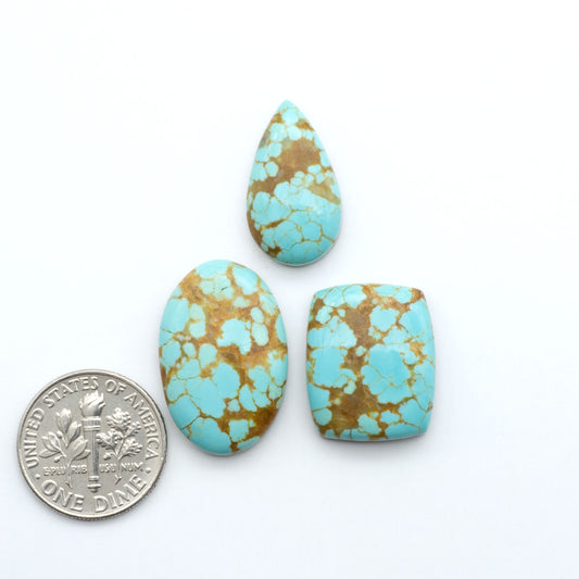Turquoise and gold marbled stones with a dime for scale on a white background. Number 8 Turquoise Cabochons have been selected for their quality and unique appearance. Don't miss the chance to add a one-of-a-kind piece to your collection.