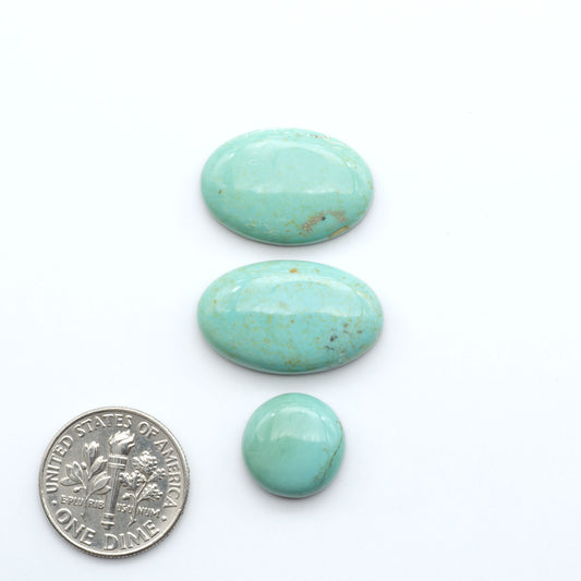 Three turquoise stones of different sizes on a white background with a dime for scale.
