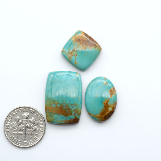 Three turquoise stones with gold veins next to a U.S. dime on a white background
