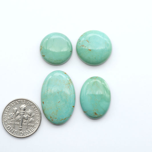 Four turquoise stones of varying sizes on a white background with a U.S. dime coin for scale.