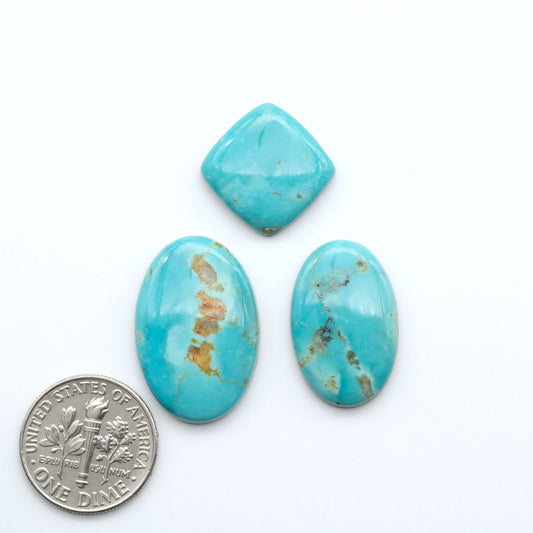 Three turquoise stones of different shapes and sizes on a white background with a dime for scale.