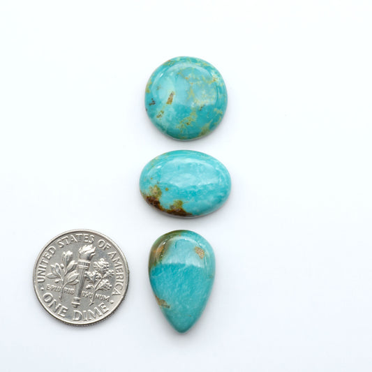 Three turquoise stones of different shapes and sizes on a white background with a dime for scale.