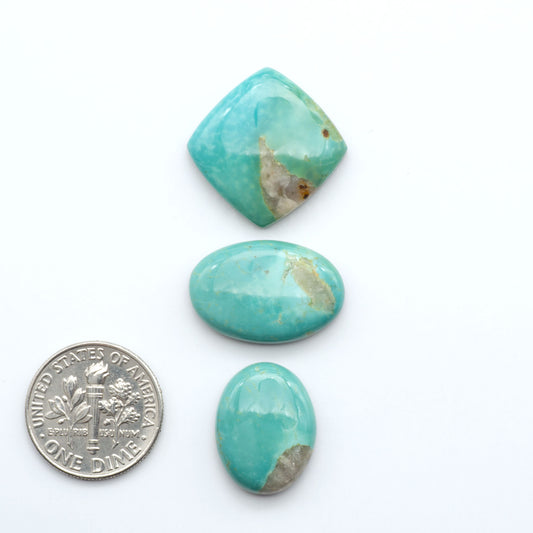 Three turquoise stones of different shapes and sizes on a white background with a dime  for scale.