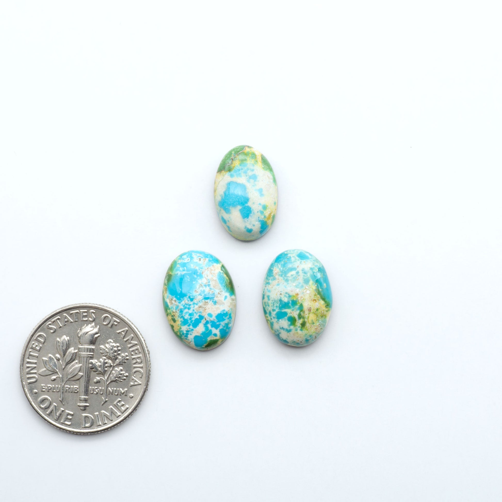 Three blue and green marbled stones next to a U.S. dime on a white background
