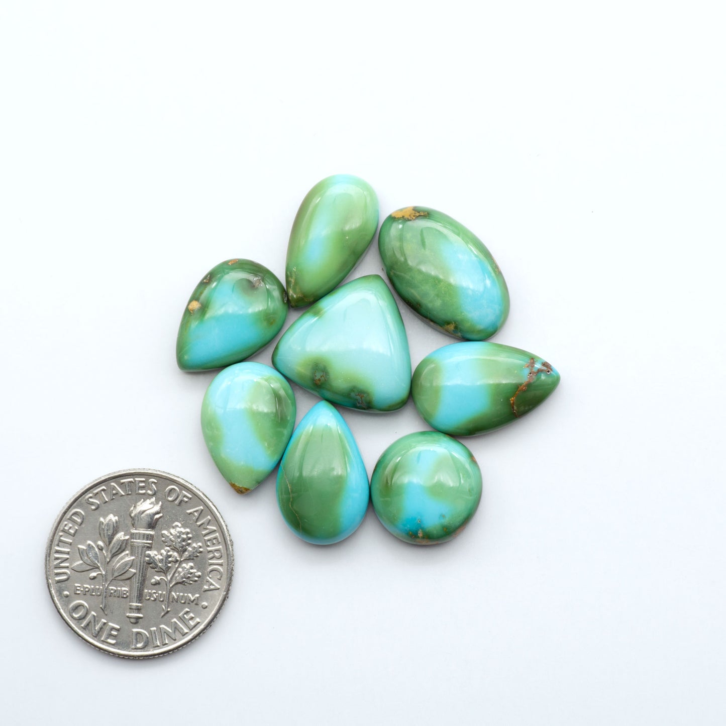 Turquoise stones with a U.S. dime for size comparison on a white background