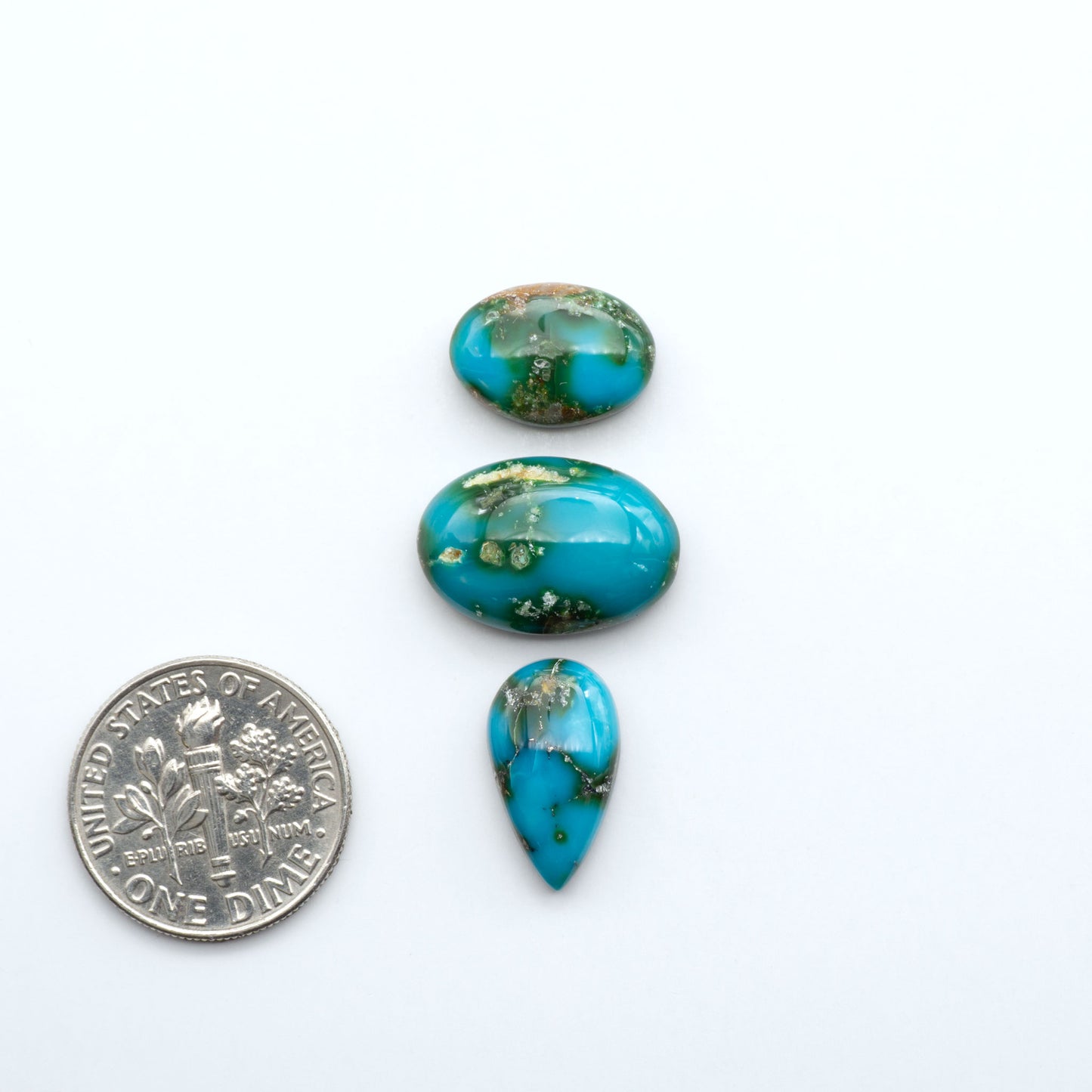 Turquoise stones of different shapes and sizes on a white background with a dime for scale.