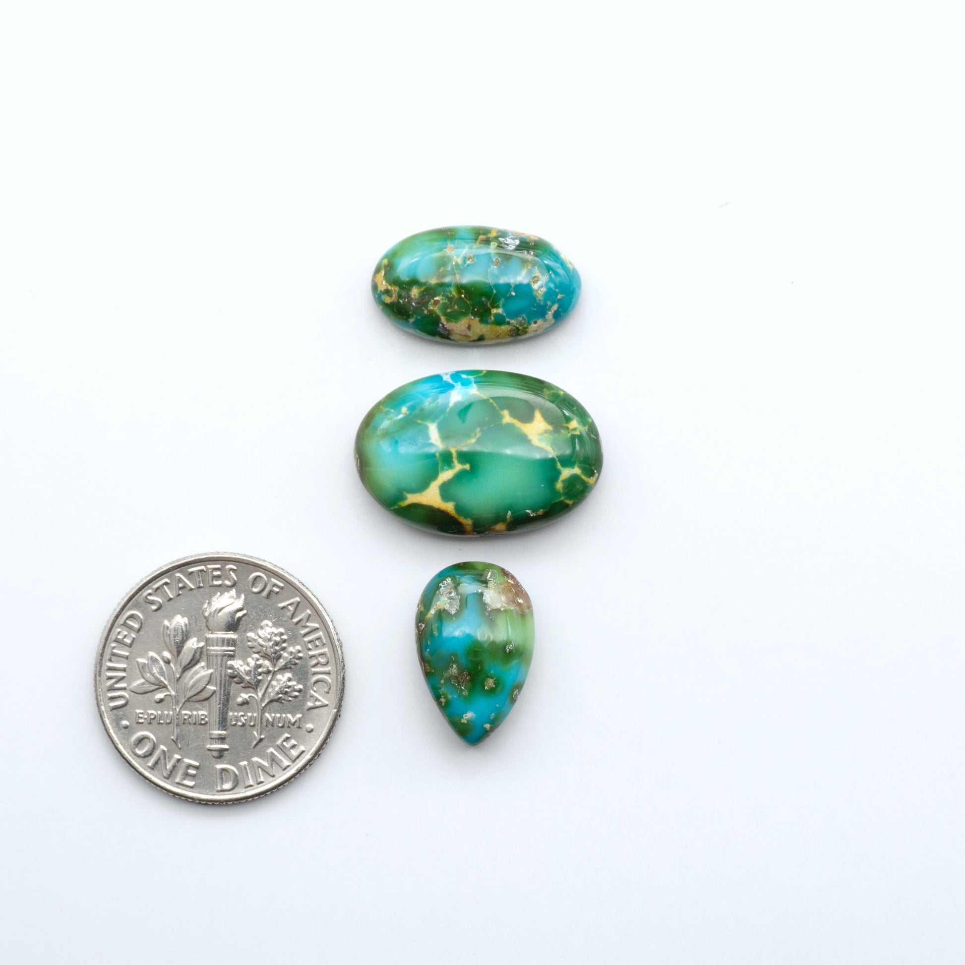 Three green and gold marbled turquoise stones with a U.S. dime for scale on a white background