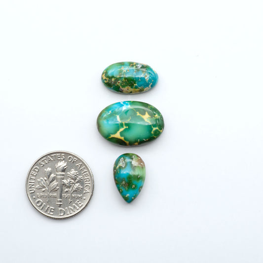 Three green and gold marbled turquoise stones with a U.S. dime for scale on a white background