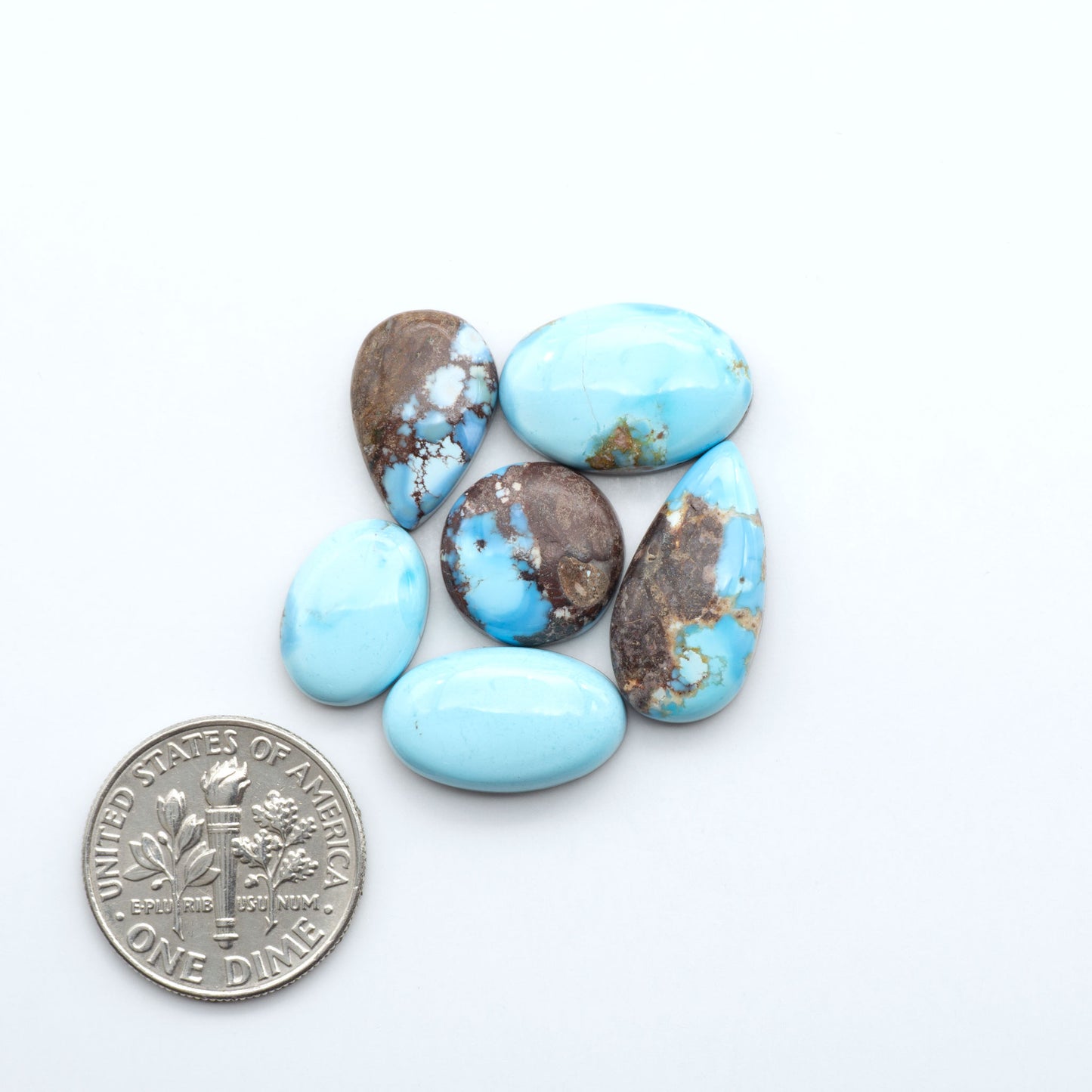 Turquoise stones with a dime for size comparison on a white background