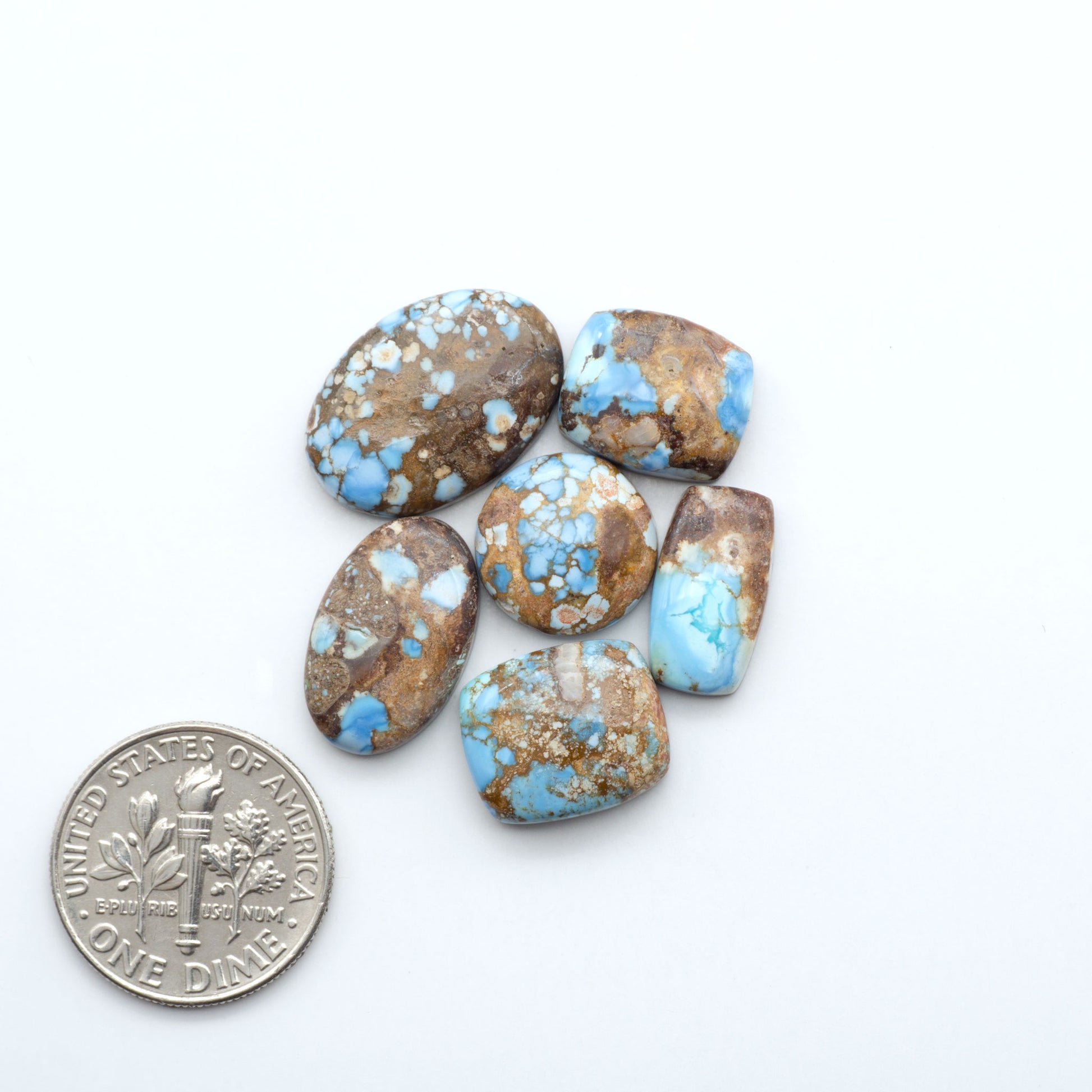 Turquoise stones with brown and blue patterns on a white background, next to a U.S. dime for scale.