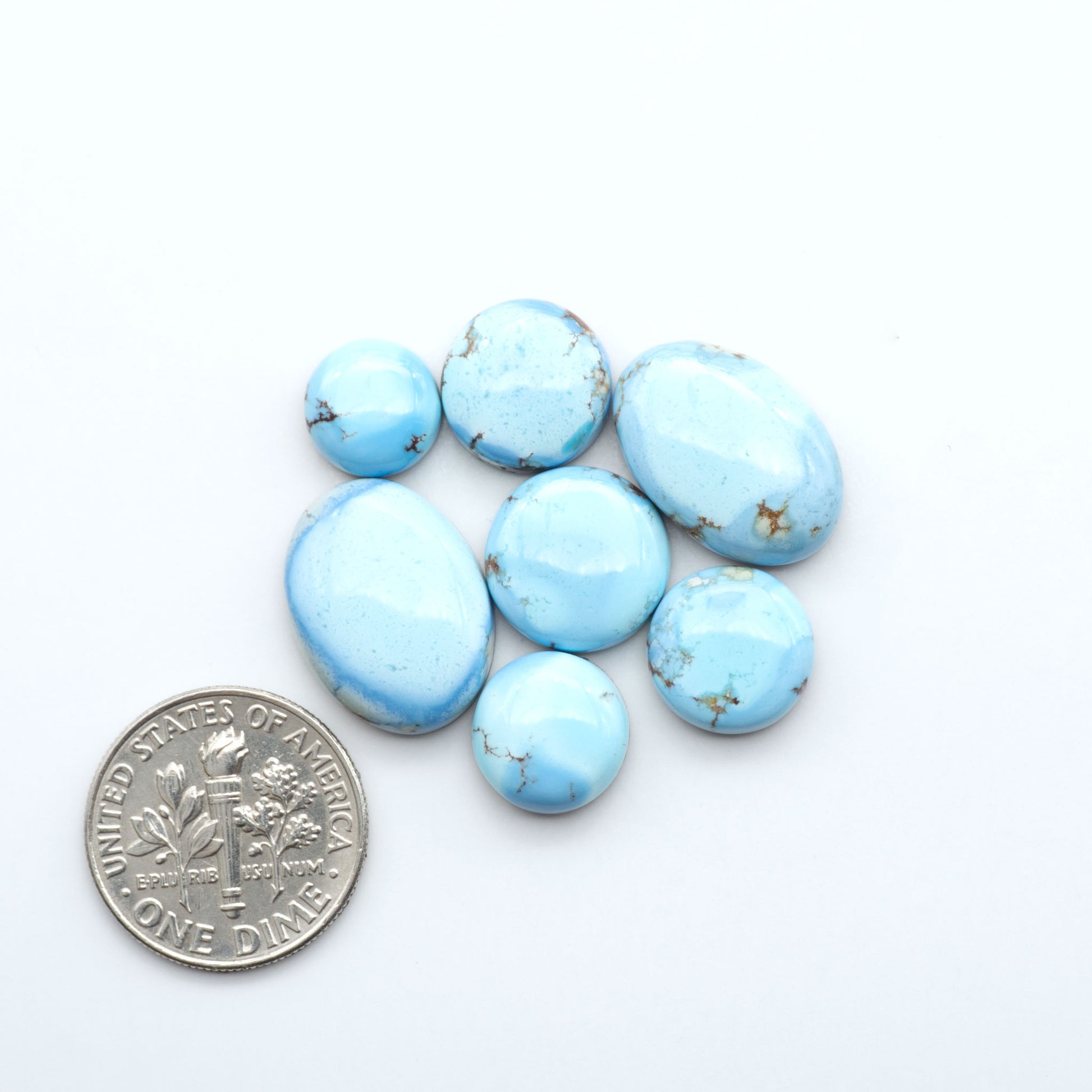 Blue turquoise stones on a white background with a U.S. dime for scale