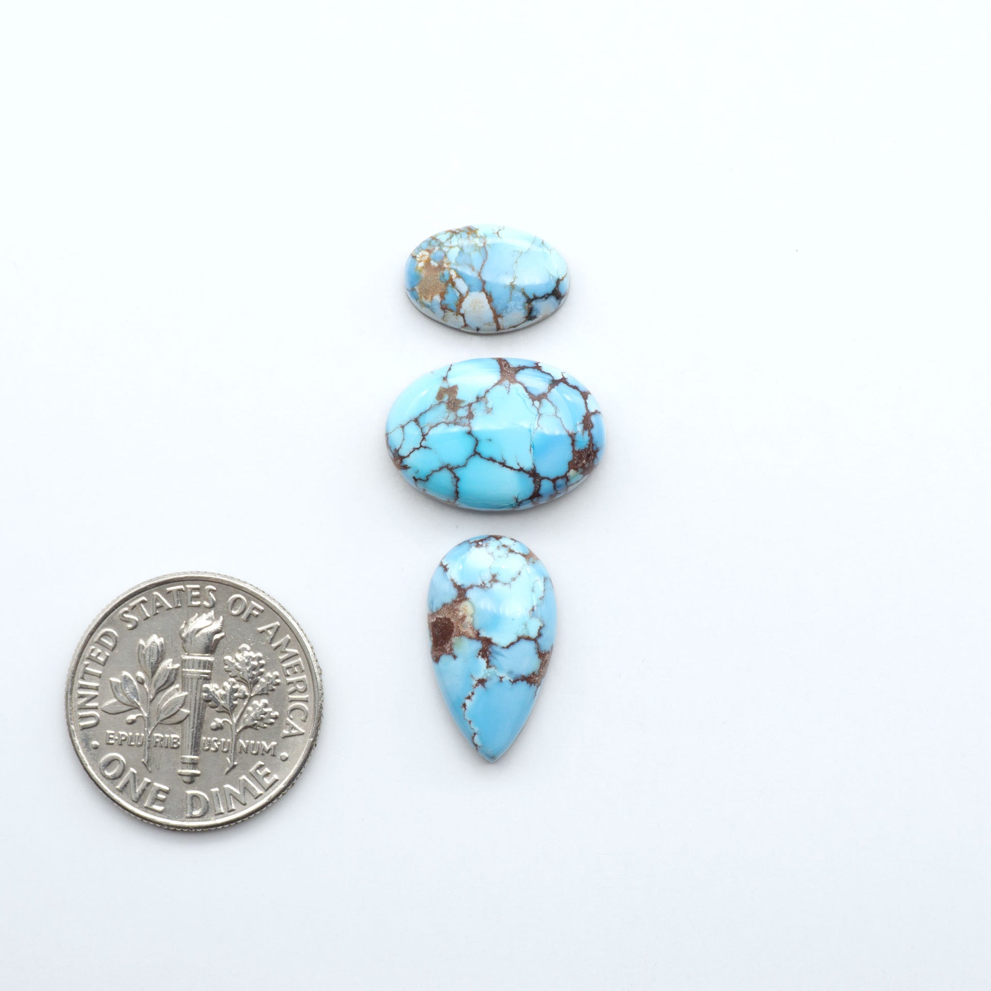 Three turquoise stones of different shapes and sizes on a white background with a dime for scale.