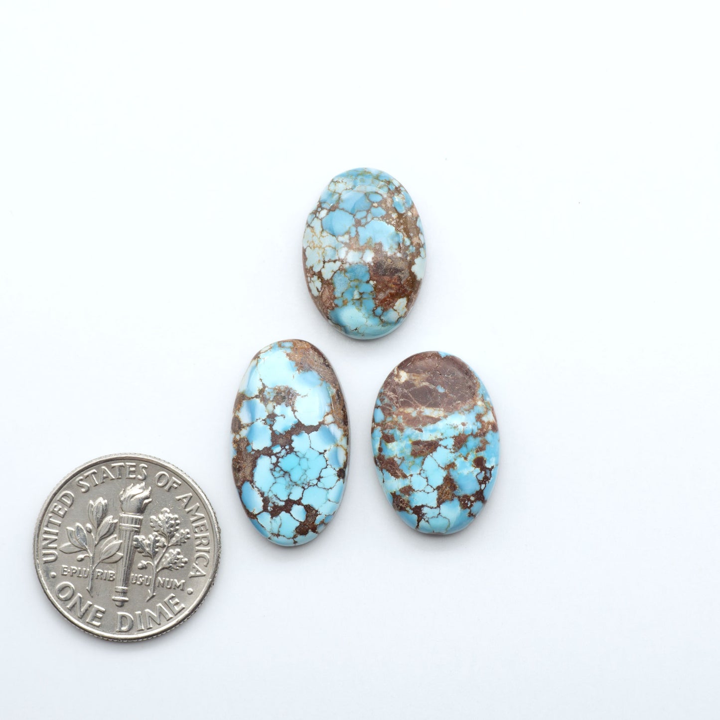 Three turquoise stones with a U.S. dime for scale on a white background