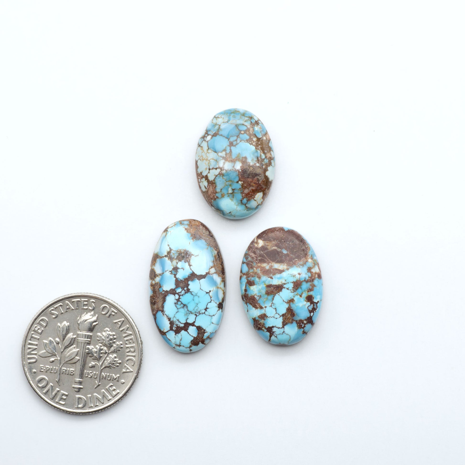 Three turquoise stones with a U.S. dime for scale on a white background