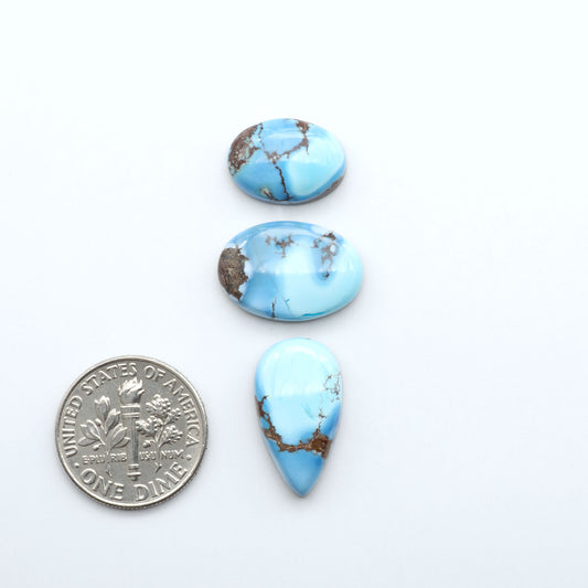 Three blue turquoise stones with brown speckles next to a U.S. dime on a white background