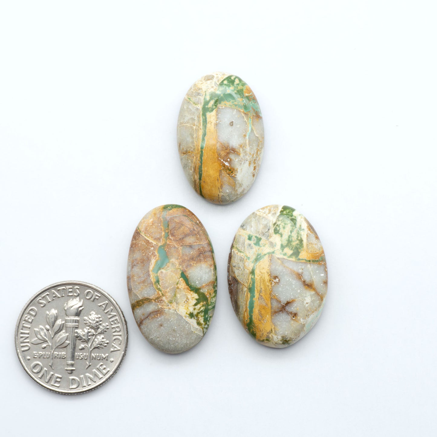 Three oval royston turquoise stones with gold and green patterns next to a U.S. dime on a white background