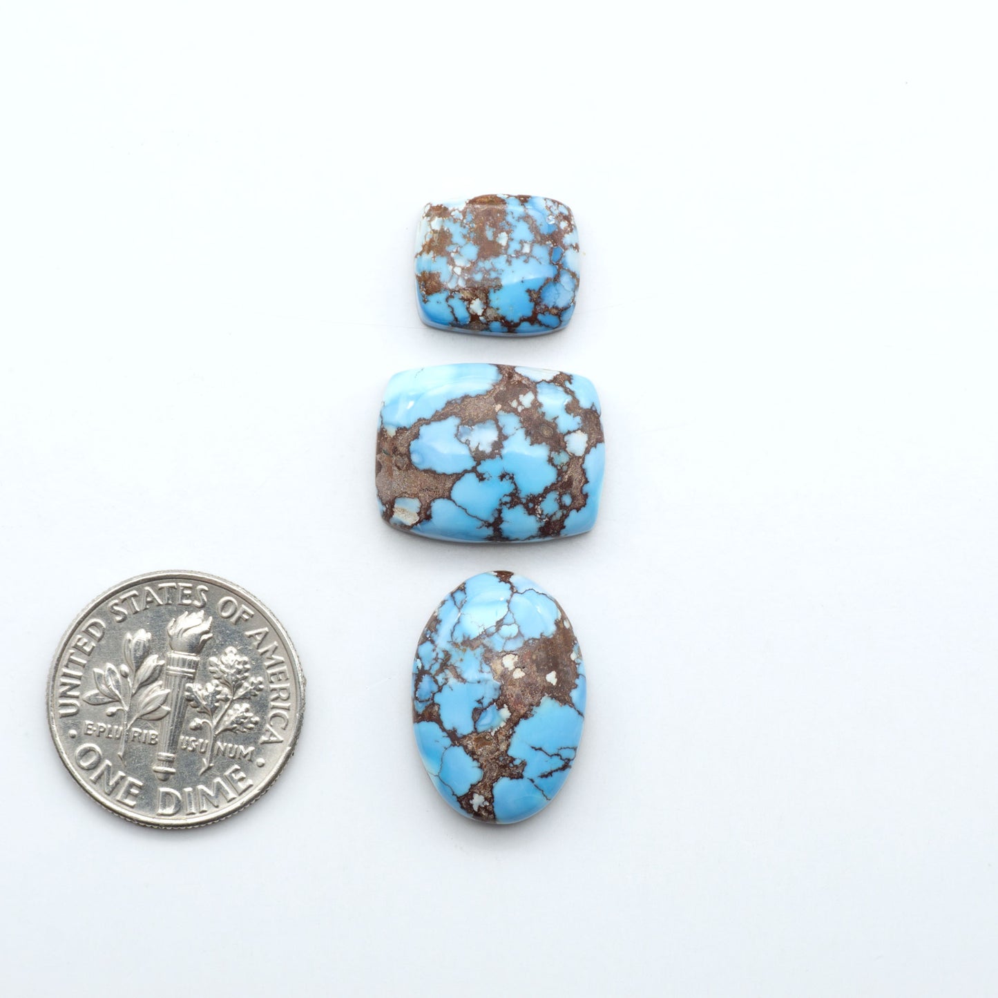 Golden Hills Turquoise cabochons, icy blue to lavender tones with chocolate matrix, polished stones on a white background with a US dime for scale