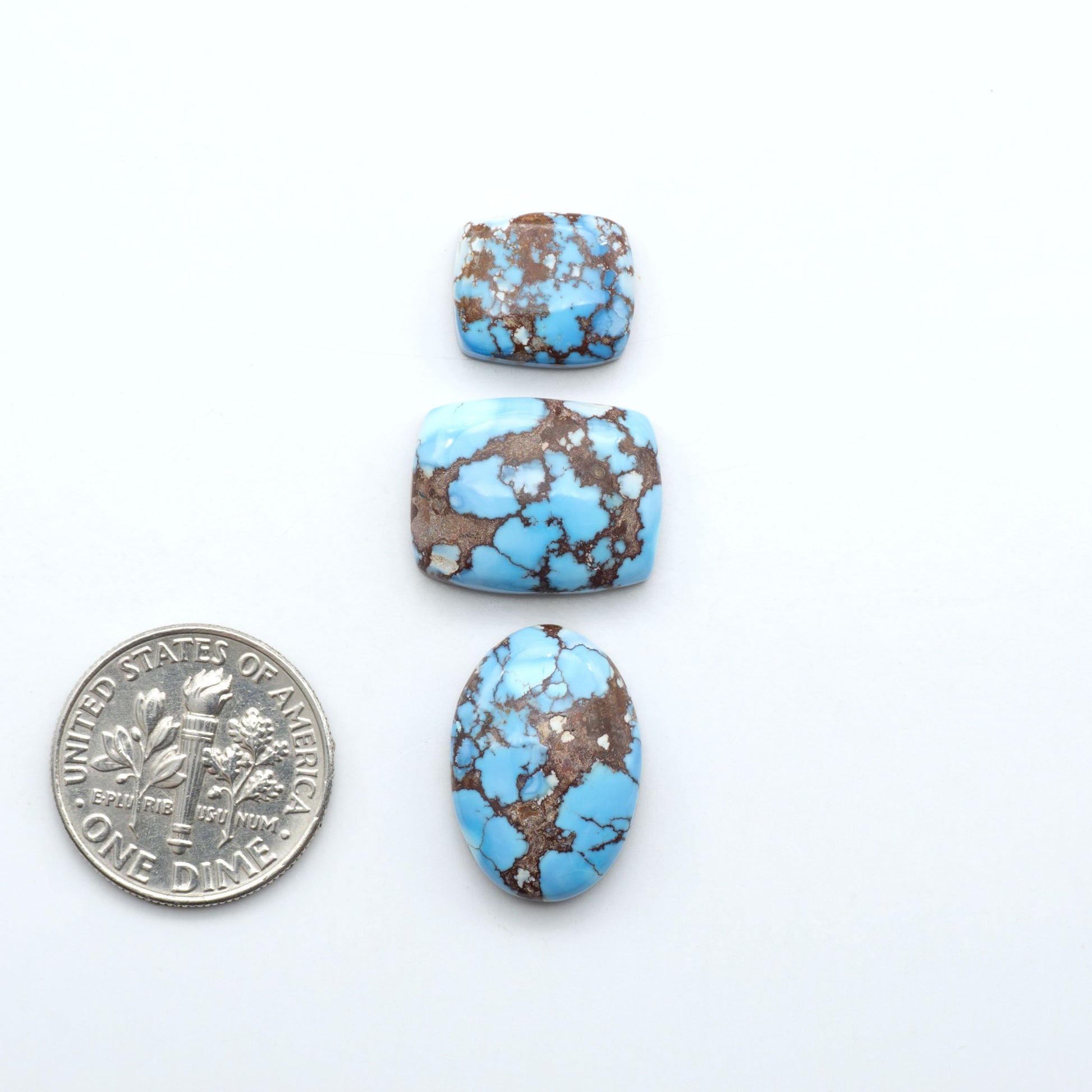 Golden Hills Turquoise cabochons, icy blue to lavender tones with chocolate matrix, polished stones on a white background with a US dime for scale