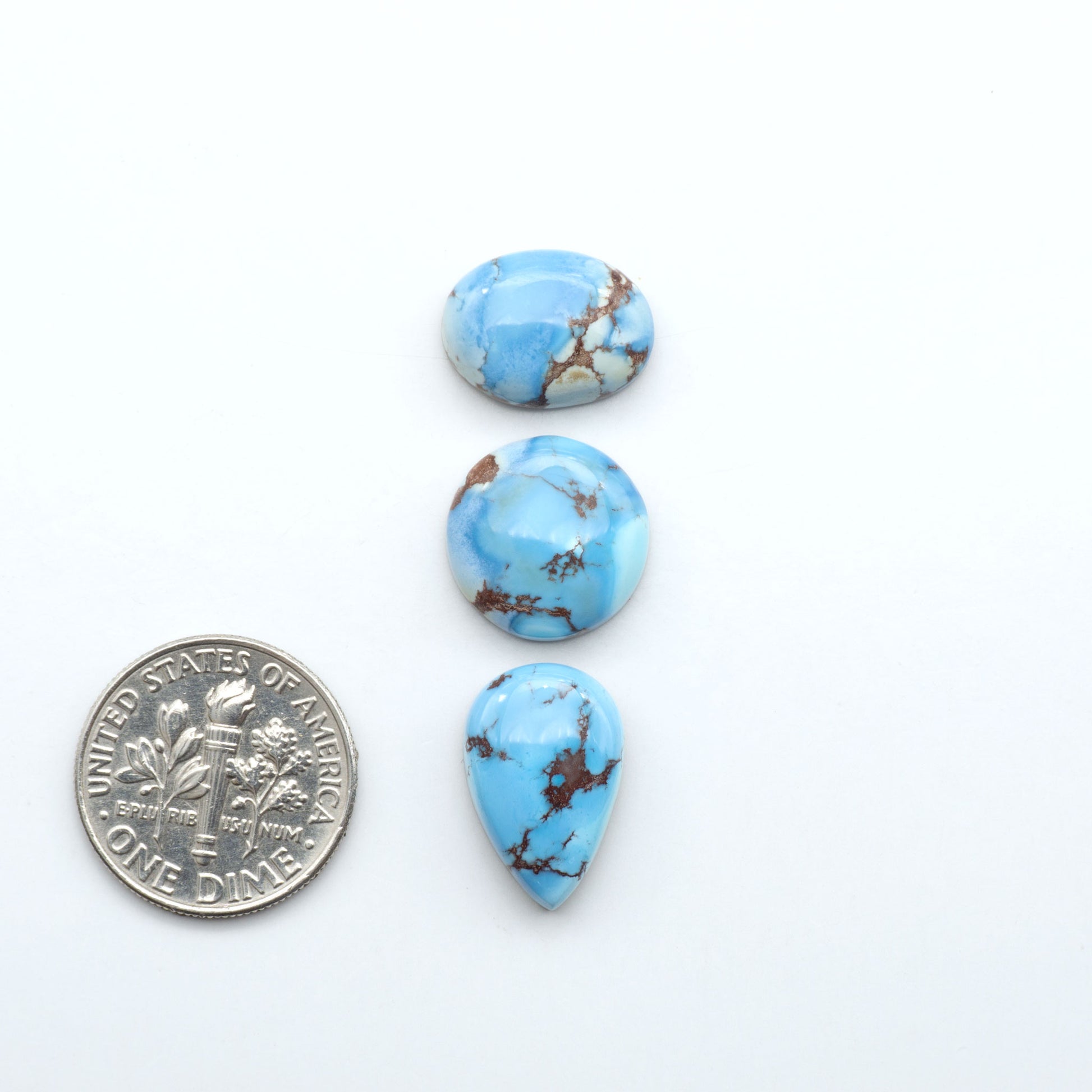 Golden Hills Turquoise cabochons, icy blue to lavender tones with chocolate matrix, polished stones on a white background with a US dime for scale