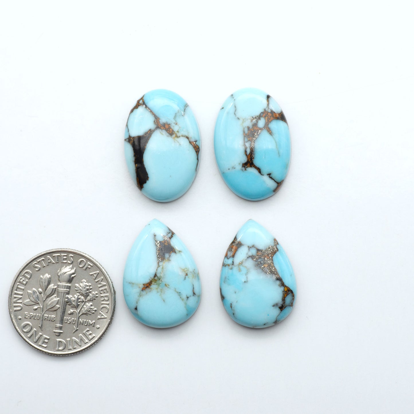 Pressed Turquoise nugget cabochons, stabilized composite with blue color and dark matrix on a white background, with a US dime for size